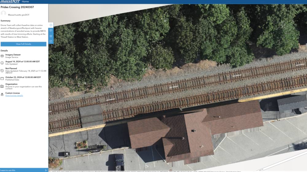 Overhead orthomosaic of MBTA rail tracks at Prides Crossing showing dual rail lines, a station building, parking area, and adjacent tree canopy.