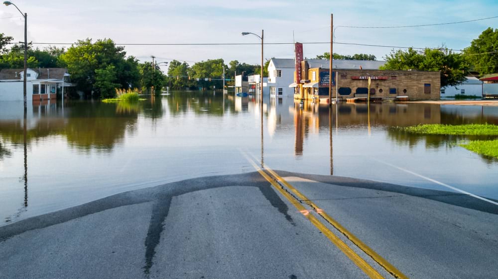 A flooded street with submerged storefronts and standing water reflecting the sky.