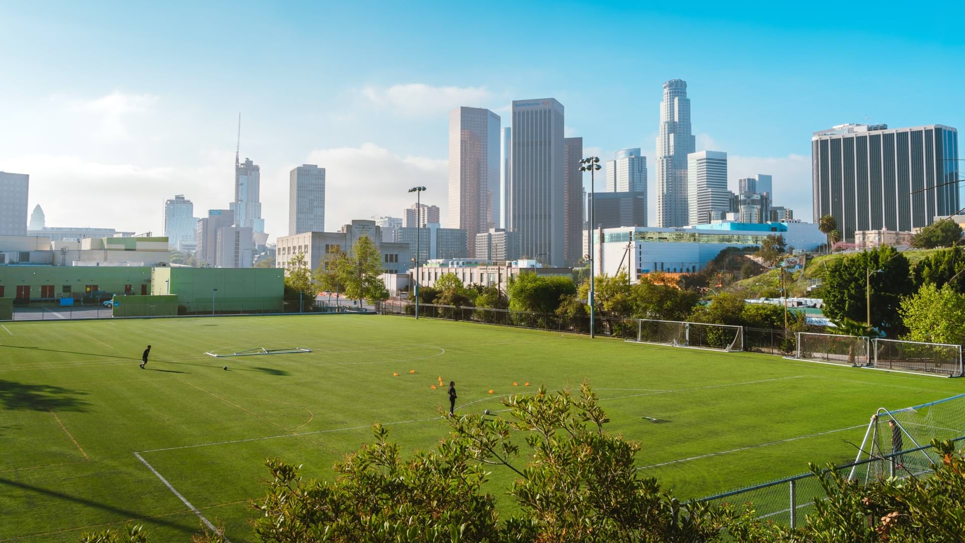 Empty soccer field with two people practicing, framed by the downtown Los Angeles skyline.