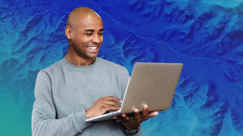 A smiling young man looking at an open laptop