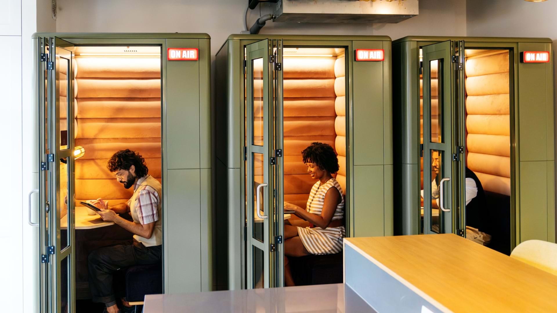Three employees sit in isloated pods in a return to office scenario