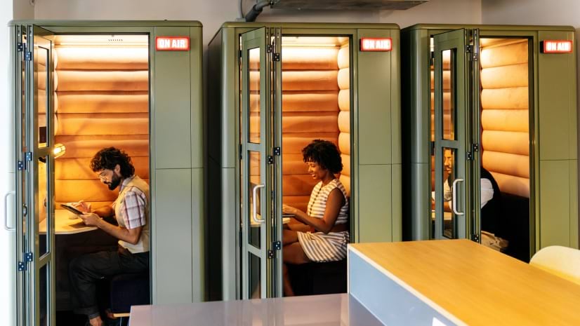 Three employees sit in isloated pods in a return to office scenario