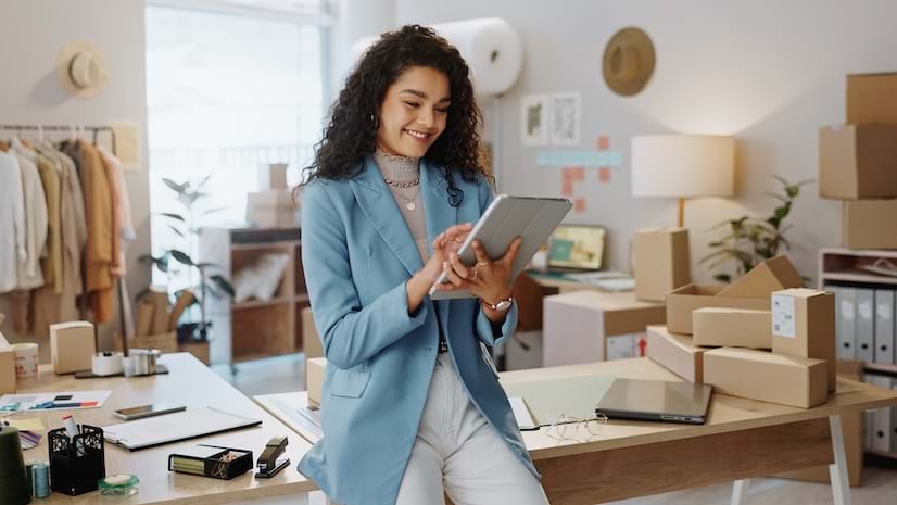 A smiling young woman leaning on a desk and using her tablet