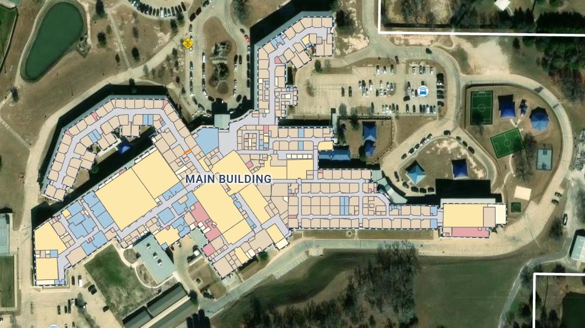 Aerial view of a high school campus with the main building outlined and its rooms and hallways drawn as color-coded shapes over satellite imagery.