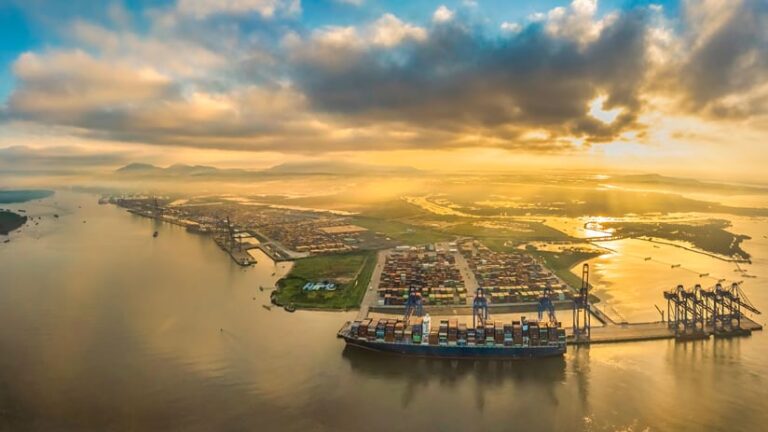 Aerial view of a large shipping port at sunrise with a container ship docked at the pier.