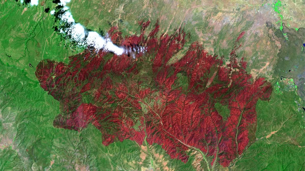 False-color satellite image showing the Rodeo-Chediski Fire's burn scar in dark red across Arizona forestland, with smoke plumes visible near the fire's edge.
