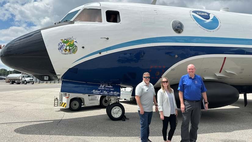 Two men and a woman standing in front of large plane on a runway