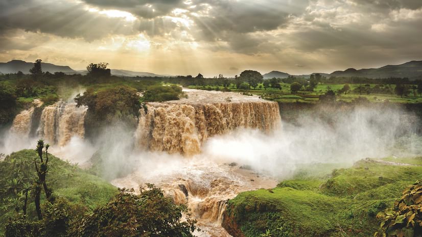A large flowing waterfall with steam rising in green forest