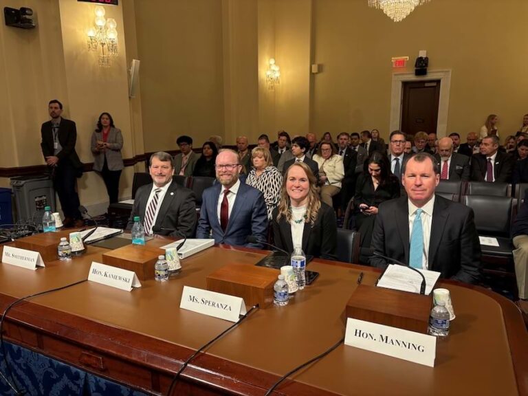 A 4-person panel at a table with mics and name tags in front of them