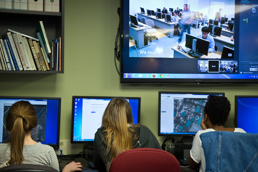 Several George Washington University students focus on creating their maps. A screen above them displays a live feed of their counterparts at George Mason University in Fairfax, Virginia, simultaneously mapping. Photo/Heather Blevins