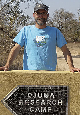 Marcel Duhaime poses in his Esri T-shirt behind a sign pointing to Djuma Research Camp