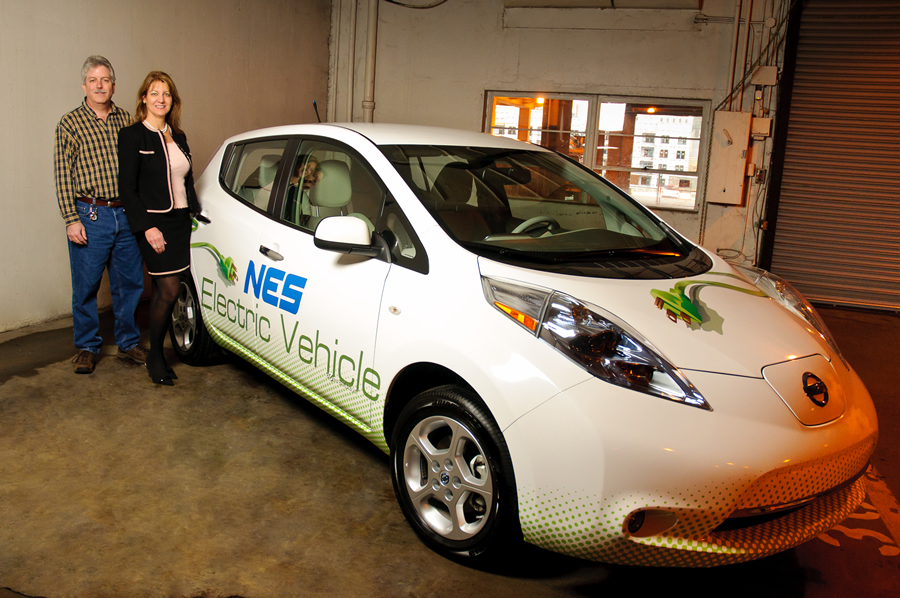 Carla Nelson and Keith Brown stand inside the NES garage with one of the electric utility's three Nissan Leaf vehicles, which were purchased as part of the market testing. Credit: Joe Weaver Photography.