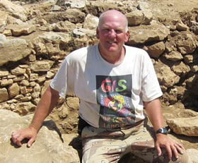 Tom Miller, GIS manager is posing with an olive press stone found at the Khirbet el-Maqatir archaeological dig in the West Bank of Israel