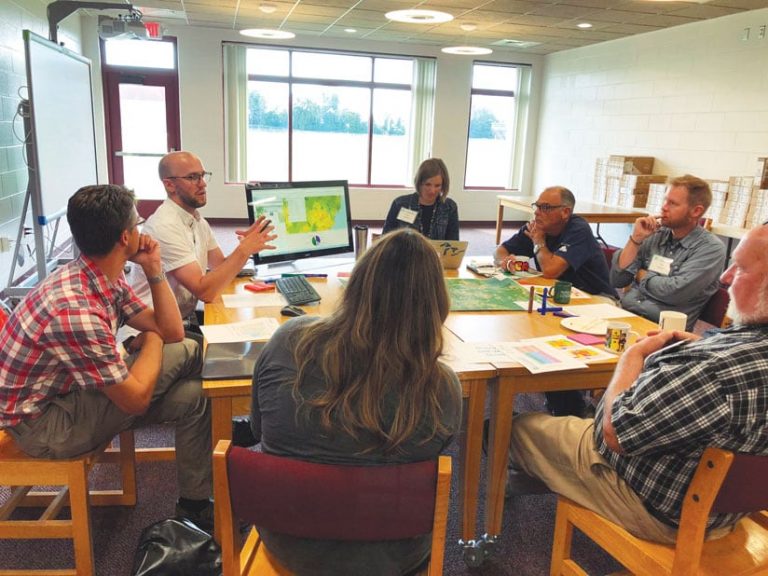 A photo of seven people sitting around a table talking A photo of seven people sitting around a table talking