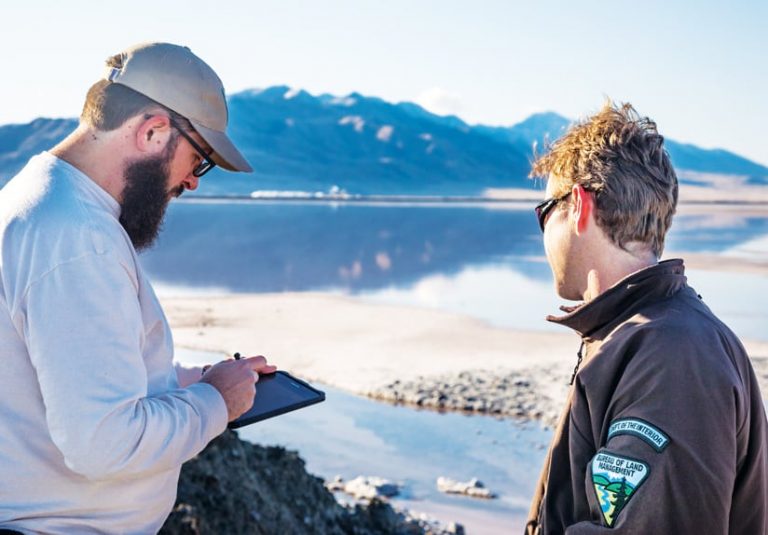 A photo of two BLM staff members using a mobile device near a lake