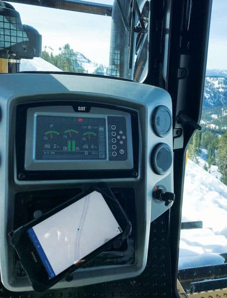 A photo from inside a bulldozer, showing the Collector for ArcGIS map on a tablet under the dashboard and piles of snow outside