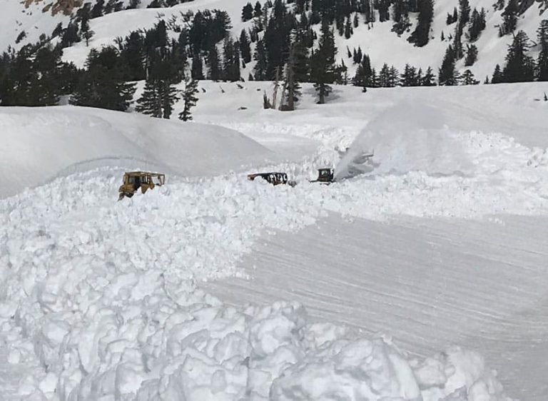 A photo of three bulldozers plowing a path through several feet of snow
