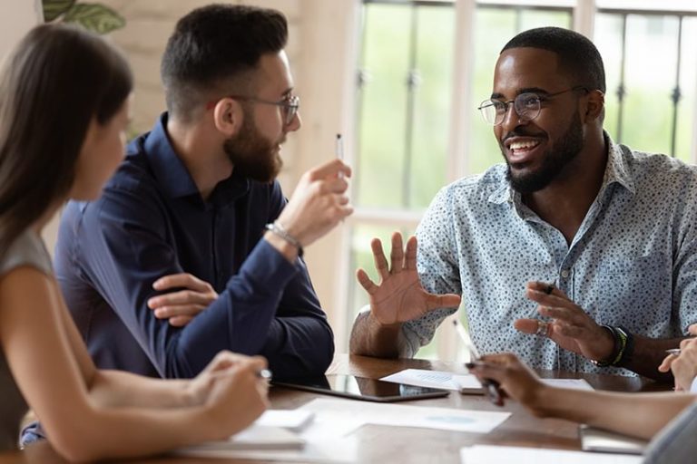 A manager sits around the table with three of his team members talking about ideas