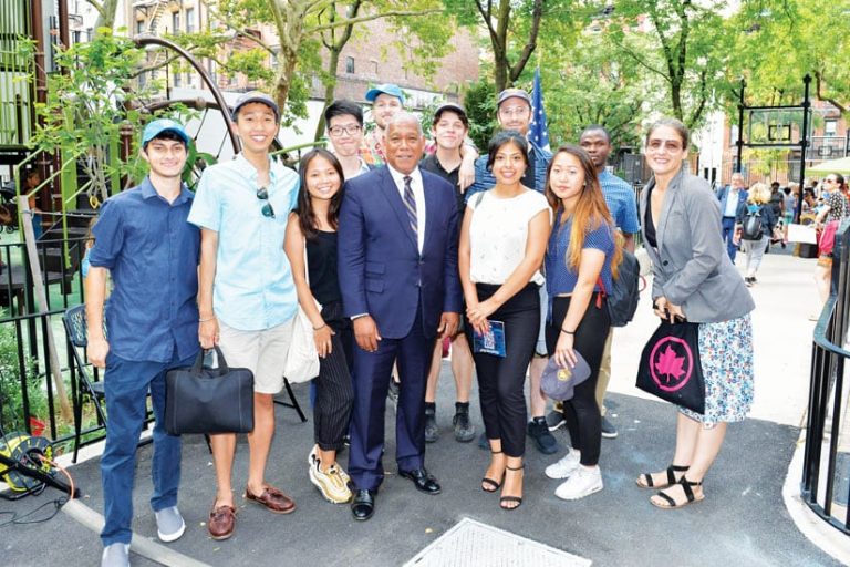 A photo of ten college-age interns standing in a park with Terese Flores and NYC Parks commissioner Mitchell J. Silver