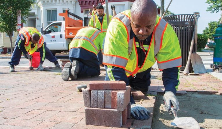 A photo of four men on laying a brick sidewalk A photo of four men on laying a brick sidewalk