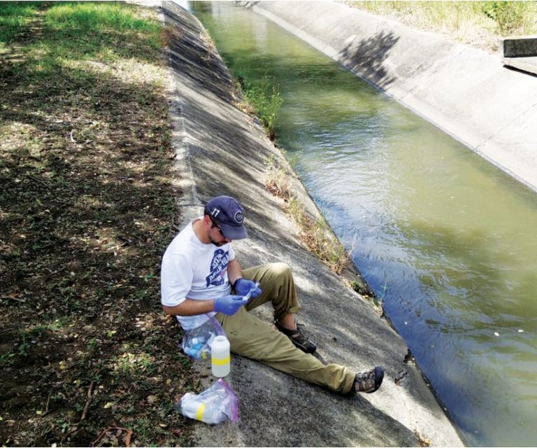 A photo of a man sitting on the side of a wash using some scientific fieldwork instruments A photo of a man sitting on the side of a wash using some scientific fieldwork instruments