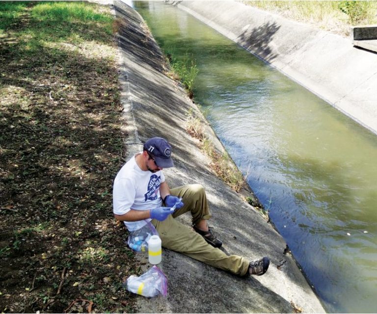 A photo of a man sitting on the side of a wash using some scientific fieldwork instruments