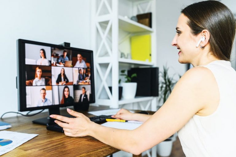 A woman sitting at a desk in her home having a video conference on her computer screen with nine other people