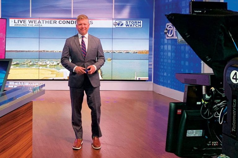 Ryan Miller in the ABC-7 television studio standing in front of a camera with a big screen behind him that says, “Live Weather Conditions”