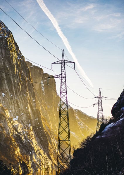 Tall power lines in between tall mountains against a blue sky