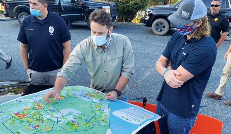 Three people wearing face maskslook at a map and one person points to a location on the map Three people wearing face maskslook at a map and one person points to a location on the map