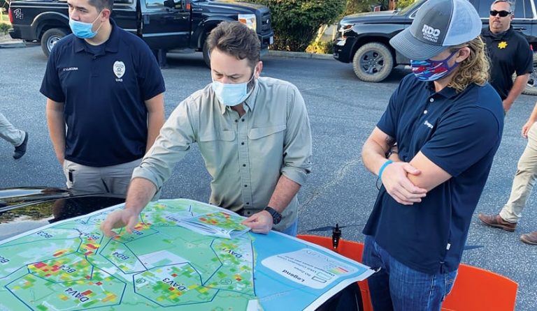 Three people wearing face maskslook at a map and one person points to a location on the map