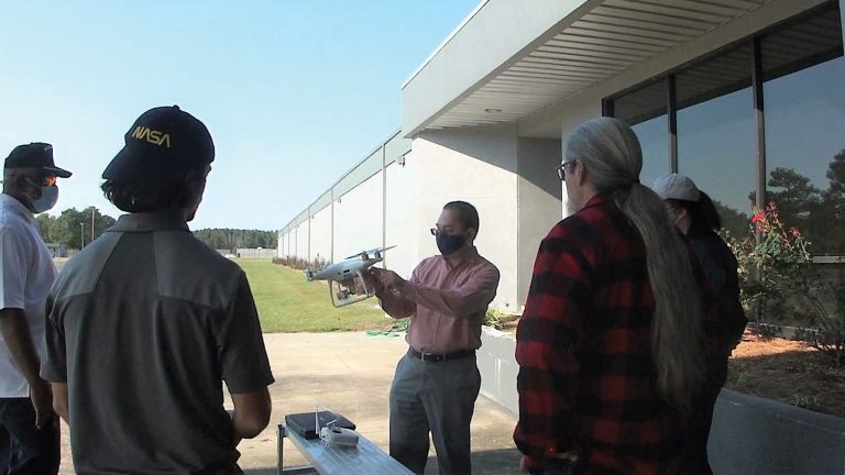 Dr. AdegokeAdemiluyi showing students a white UAV outside of a building Dr. AdegokeAdemiluyi showing students a white UAV outside of a building
