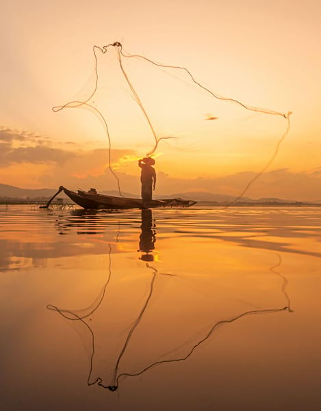 A silhouette of a fisherman in a boat on a freshwater water river at sunset