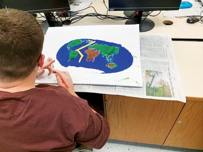 Student sitting at a desk working on a physical 3D map Student sitting at a desk working on a physical 3D map