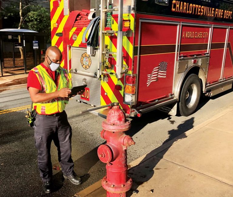 A firefighter standing next to a fire hydrant using a tablet to record an inspection