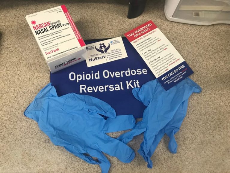 An opioid overdose reversal kit, with a box of Narcan (naloxone), latex gloves, a brochure, and a business card