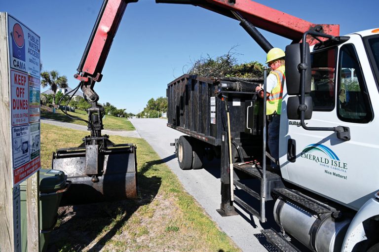 A yard waste truck with a driver in it picks up some yard debris