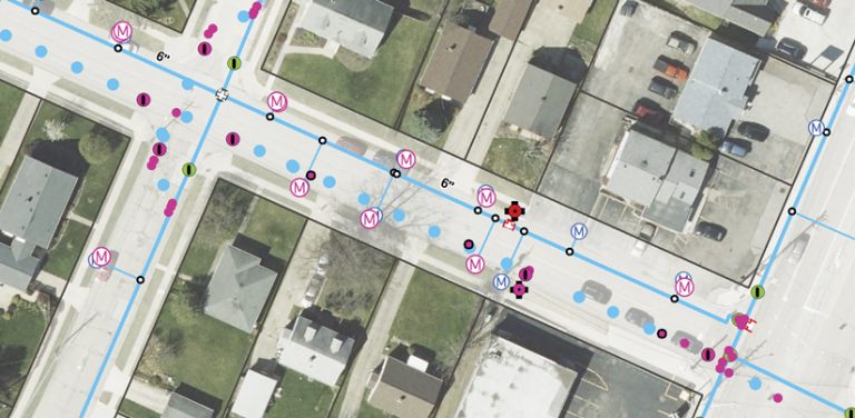 An aerial image of a residential neighborhood with blue lines; blue, pink, and green dots; and pink and purple Ms that indicate various utility assets An aerial image of a residential neighborhood with blue lines; blue, pink, and green dots; and pink and purple Ms that indicate various utility assets