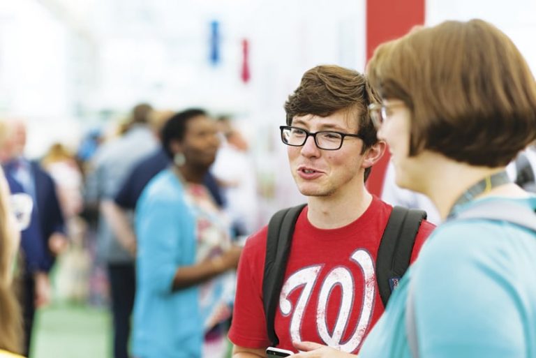 A young person talking to others in a small group at a conference A young person talking to others in a small group at a conference