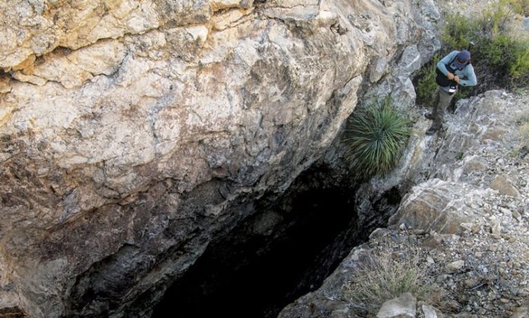 A man standing outside a vertical entrance to a cave