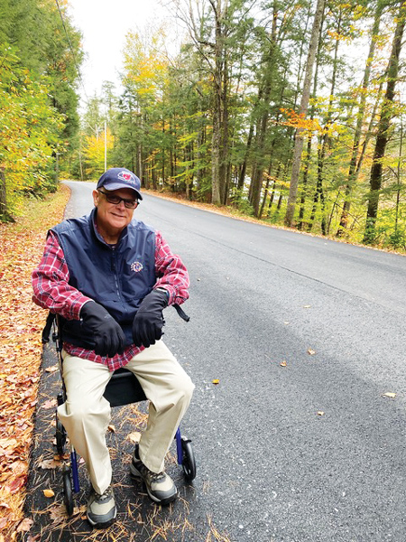 A man sitting on a walker on a rural road in the woods
