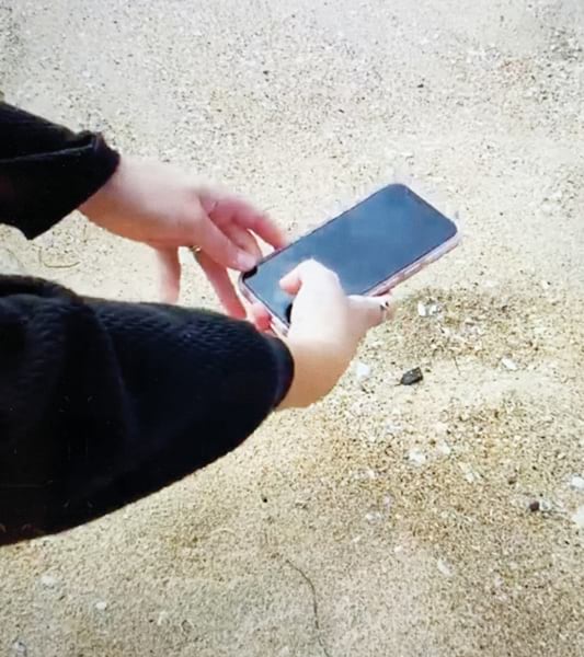 A person using a smart phone to take a photo of a tar ball on the beach