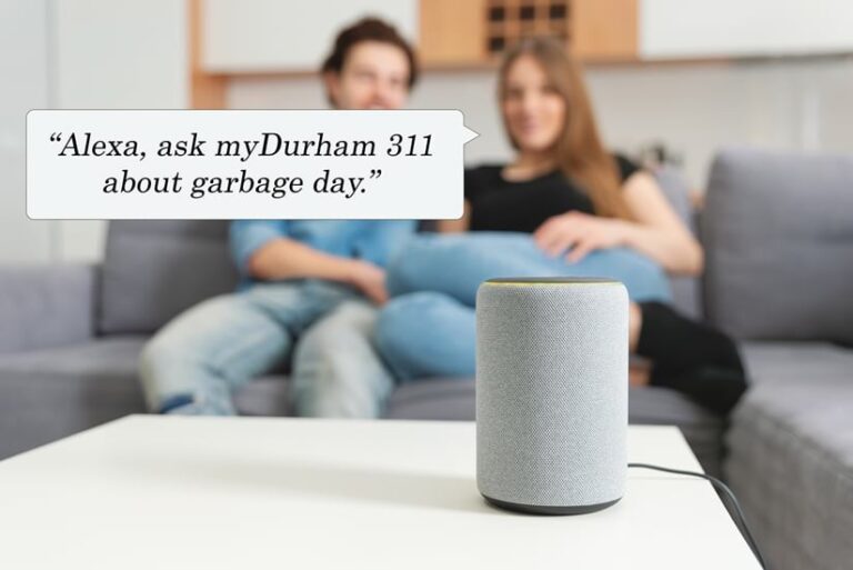 Two people sitting behind a smart home device with a speech bubble that says, “Alexa, ask myDurham 311 about garbage day”
