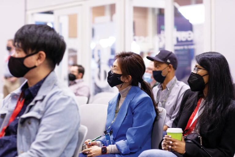 Several attendees in black masks sitting in chairs listening to a presentation