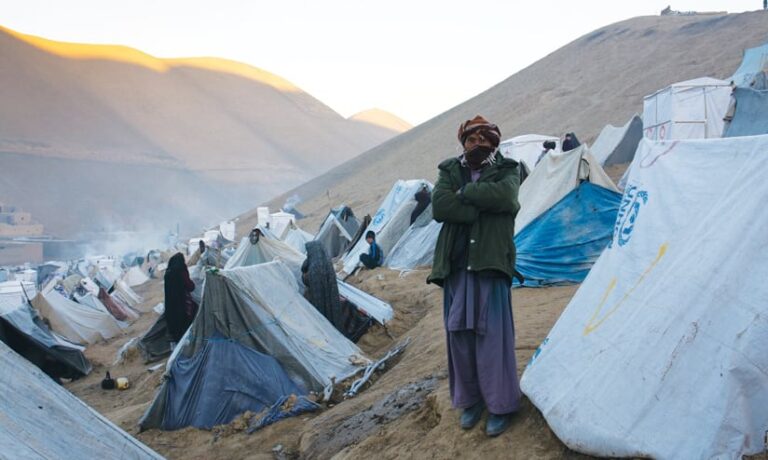 A man standing in front of tents in a refugee camp