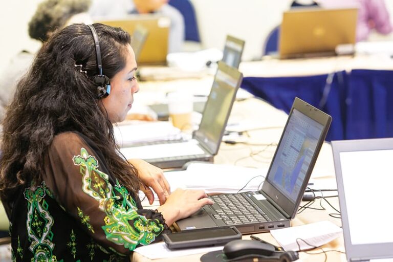 A woman at a laptop with headphones on in a room with other people at laptops