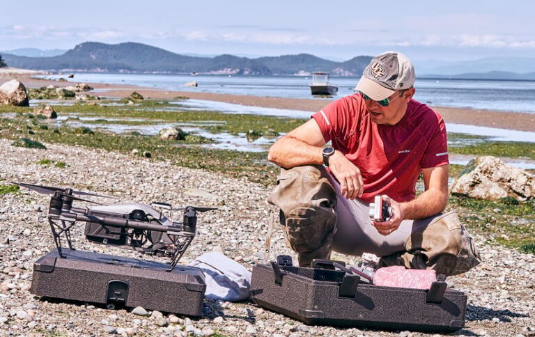 Tim Hawthorne kneeling next to a drone on a rocky beach