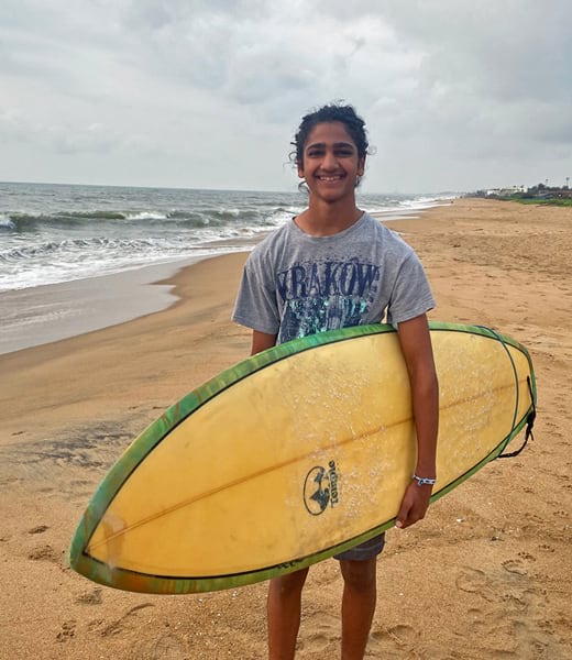A teenager standing on a beach holding a surfboard