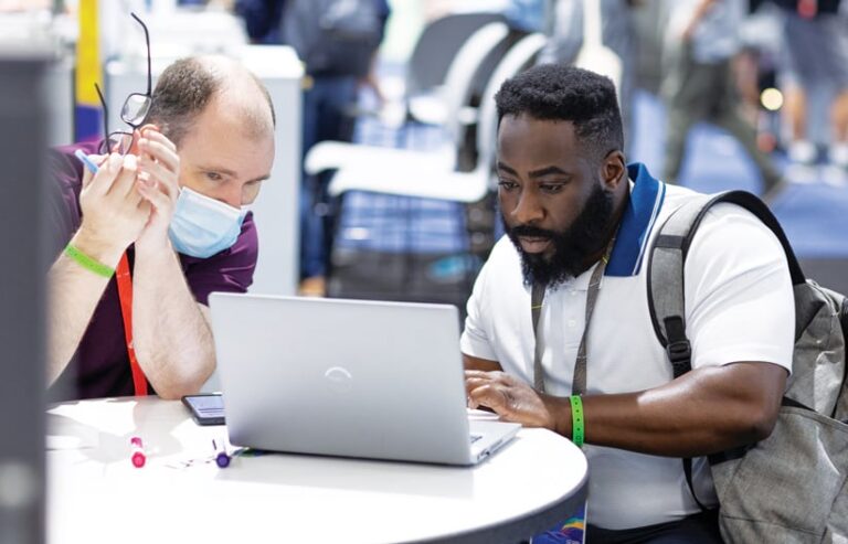 Two men sitting at a small table looking at a laptop