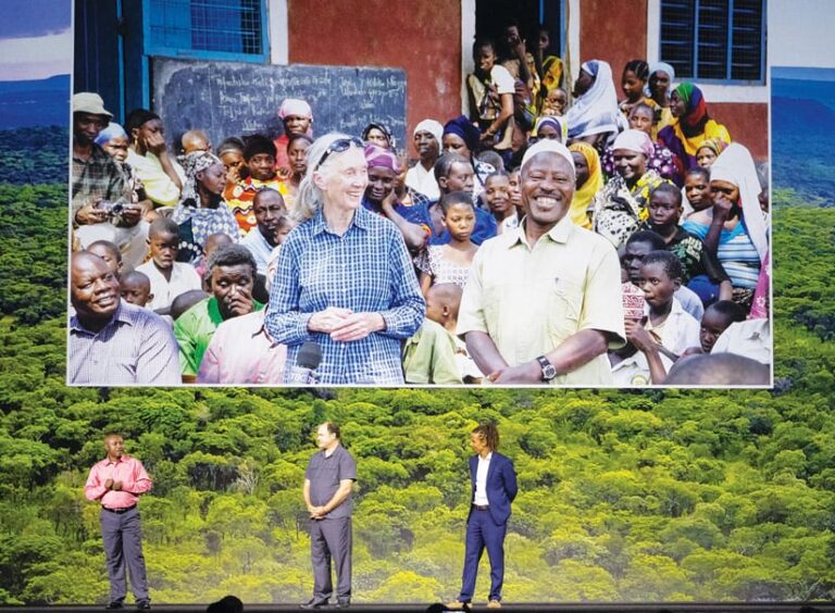 Three men presenting onstage with a photo of Jane Goodall in a crowd in the background